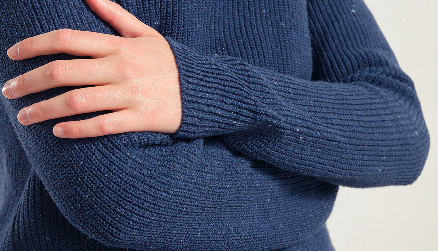 Close-up of a person wearing a blue knitted sweater with a neutral background